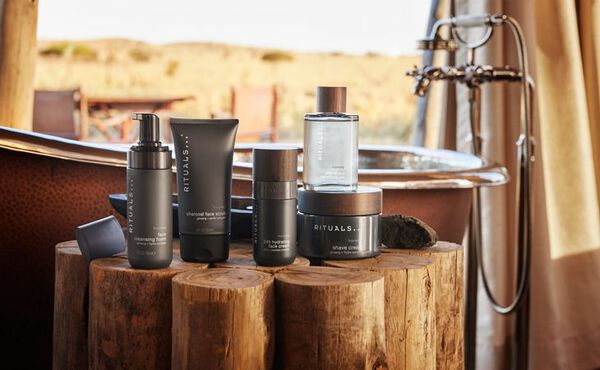 Rituals Homme collection with sleek grey packaging, displayed in a rustic outdoor bathroom setting.
