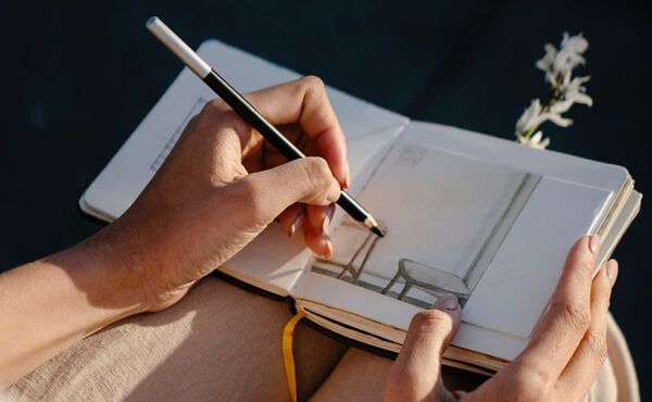 A person sketches a calming scene in a notebook, using creativity and reflection as tools for mindfulness and joy.