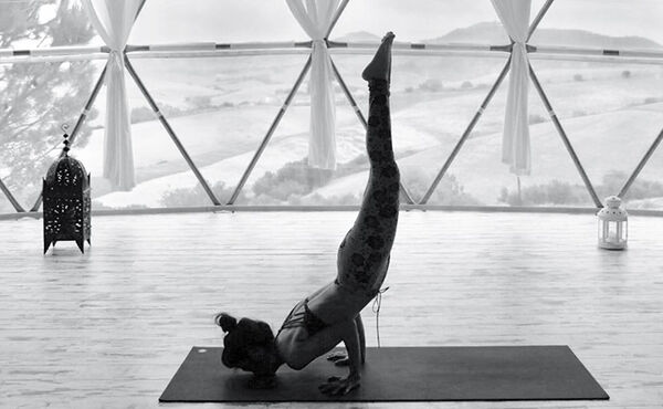 A girl on a yogamat doing a low handstand