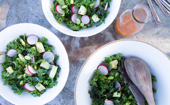 Three bowls of fresh kale and wakame salad with radish, avocado and dressing, ready to serve.