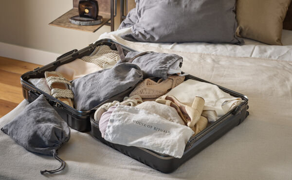 Open suitcase on a neatly made bed, filled with clothing and accessories packed in upcycled Rituals bedlinen bags.