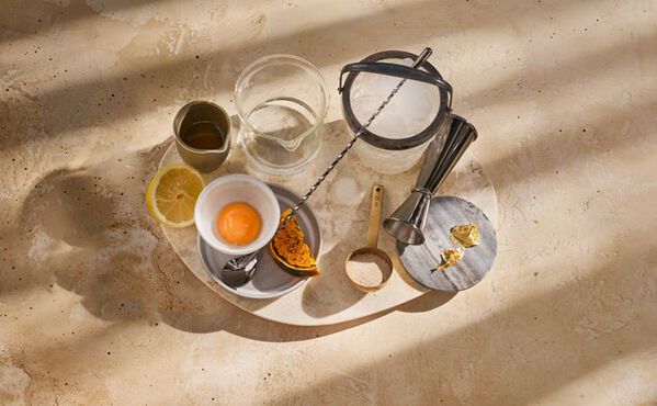 Ingredientes de cocktail de gin sem álcool, incluindo gema de ovo, limão, abóbora e especiarias, dispostos num tabuleiro pronto a misturar.