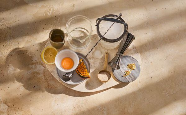 Ingrediensene til en gin sour mocktail, deriblant eggeplomme, sitron, gresskar og krydder, arrangert på et bord og klare til å blandes.