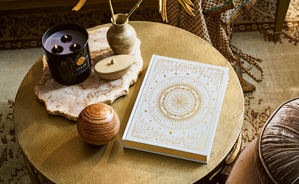 The Book of Rituals decorative coffee table book, shown on a table with a Rituals Private Collection large scented candle.