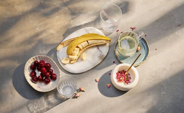 Fresh ingredients for a glowing skin smoothie recipe, including banana, cherries, rose petals and lemon juice.