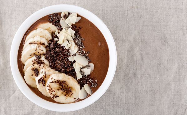 Chocolate smoothie bowl topped with banana, chia seeds and shaved chocolate, served in a white bowl.