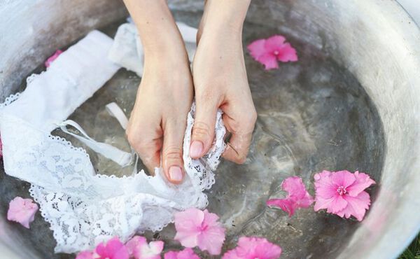 A person hand-washing delicate lace in a basin with flower petals – a calming spring cleaning tradition.