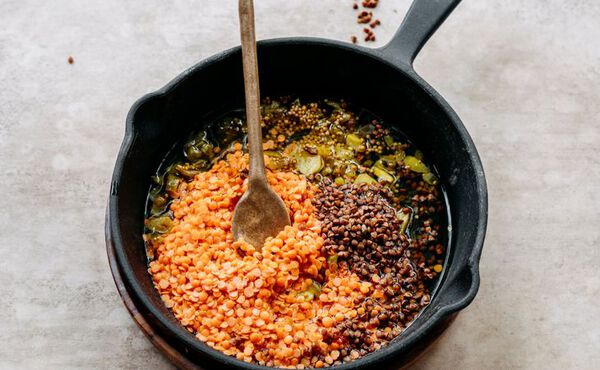 Red and black lentils cooking with spices in a cast iron skillet for a healthy meal.