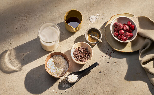Ingredients for a nourishing rice pudding recipe, including plant milk, rice, cherries, cacao nibs and almond butter.