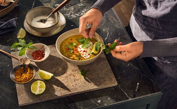 Person garnishing a bowl of kitchari with lime, mint and coconut yoghurt. A nourishing Ayurvedic comfort dish.