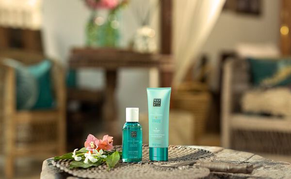 Dois produtos mini The Ritual of Karma em tamanho de viagem, apresentados numa mesa com flores, num cenário de férias de verão descontraída.