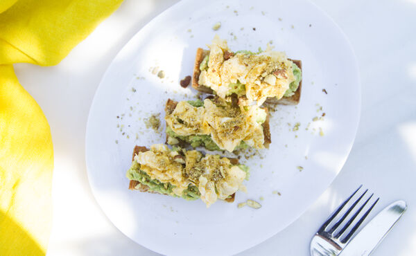 Wholegrain toast topped with avocado and scrambled eggs, sprinkled with seeds for a healthy breakfast.
