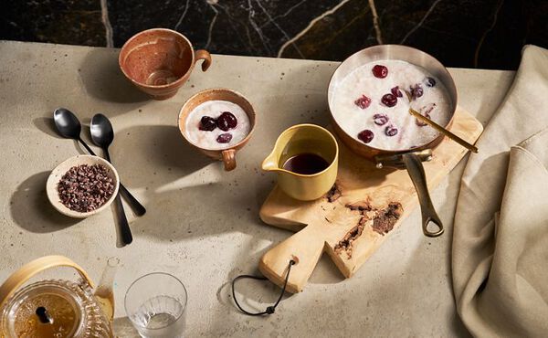 A warm bowl of rice pudding topped with cherries, served with cacao nibs and maple syrup for a wholesome breakfast.