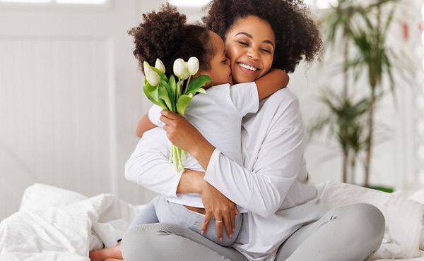 Smiling mother hugging her child who is holding white tulips, sharing a tender moment of love and kindness.