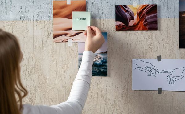Woman placing a sticky note labelled “nature” on a vision board – a creative step towards setting mindful intentions.