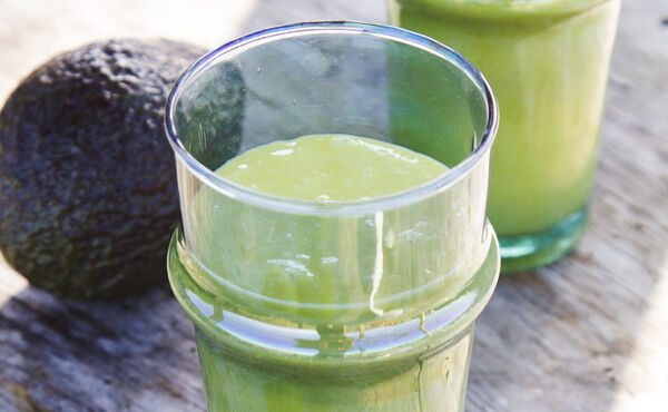 Glass med kremete grønn avokadosmoothie på en rustikk overflate - en nærende oppskrift for strålende hud.