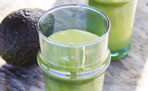 Glasses of creamy green smoothie with avocado on a rustic surface – a nourishing recipe for glowing skin.