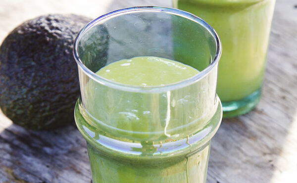 Copos de smoothie verde cremoso com abacate numa superfície rústica, uma receita nutritiva para pele radiante.