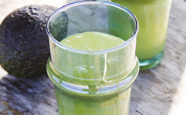 Ein Glas mit cremigem grünem Smoothie mit Avocado auf einer rustikalen Oberfläche – ein nahrhaftes Rezept für strahlende Haut.