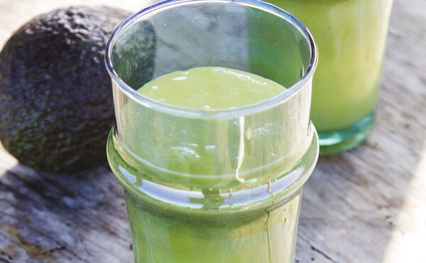 Glazen romige groene smoothie met avocado op een rustieke ondergrond - een voedzaam recept voor een stralende huid.