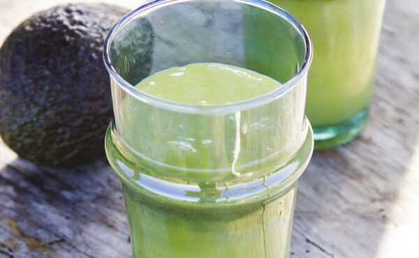 Verres de smoothie vert crémeux à l’avocat sur une surface en bois brut, une recette nourrissante pour favoriser l’éclat du teint.