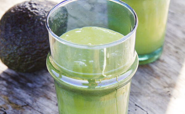 Vasos de smoothie verde y cremoso con aguacate sobre una superficie rústica, en una receta nutritiva que favorece una piel radiante.