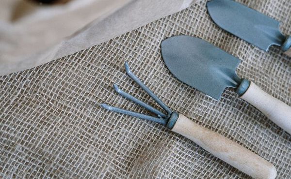 Small gardening tools with wooden handles laid out on coarse burlap fabric.