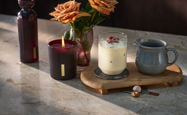 The Ritual of Ayurveda mocktail served on a wooden board, styled with warm-toned flowers and a matching scented candle.