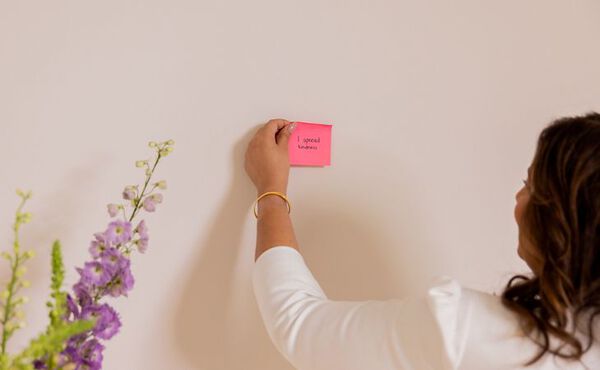 A woman sticks a pink note reading “I spread kindness” on a wall as part of a purpose-finding exercise.