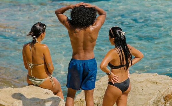 Tre venner i badetøj slapper af ved havet, nyder solskin, forbindelse og ubekymrede sommerøjeblikke sammen.