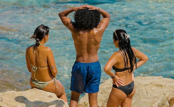 Drie vriendinnen in badkleding ontspannen aan zee, samen genietend van de zon, verbondenheid en zorgeloze zomermomenten.