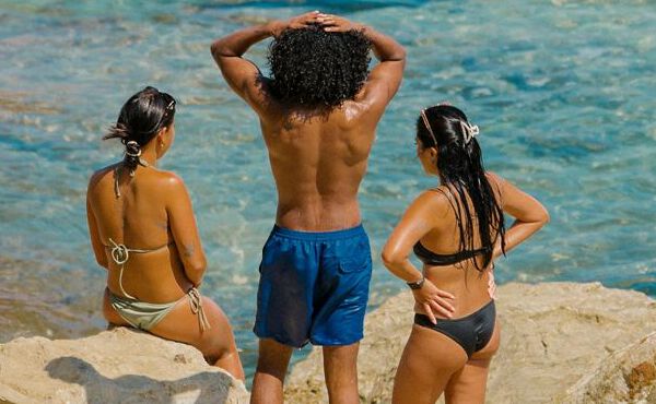 Tre vänner i badkläder kopplar av vid havet och njuter av solskenet, gemenskapen och sorglösa sommarstunder tillsammans.