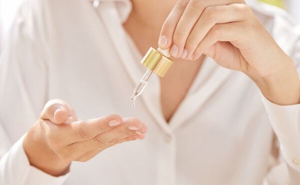 Close-up of hands dispensing a Rituals natural booster serum with a dropper, as part of a daily skincare routine.