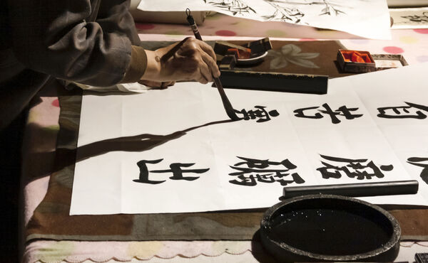 Person painting Japanese calligraphy with a brush, pactising mindfulness through traditional art.