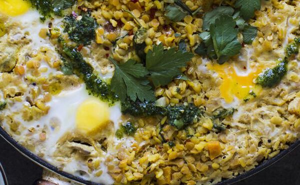Close-up of a skillet filled with baked eggs, lentils, herbs and green sauce, a hearty savoury breakfast dish.
