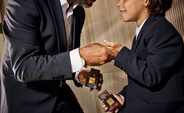 A father and son are both dressed in black suits. The father is holding the son’s hand, in both other hands they are holding Rituals perfume for men.