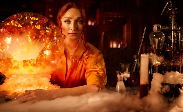 A woman in an amber-lit lab with a glowing crystal ball and alchemy tools, symbolising life transformation.