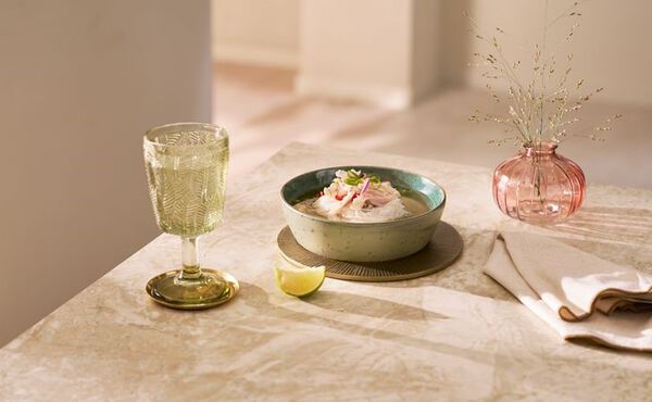 Bowl of comforting chicken pho topped with herbs and lime, served with a glass of water and linen napkin.