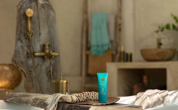 The Ritual of Karma after-sun serum placed by a bath in a calming spa-inspired bathroom.