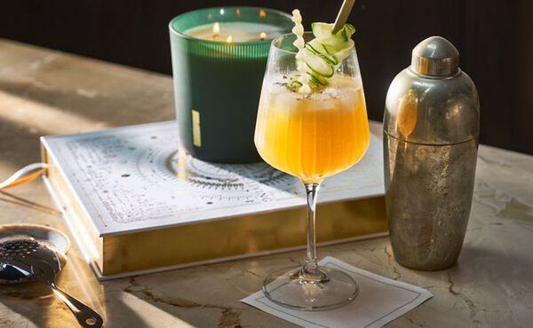 The Ritual of Jing mocktail with cucumber garnish, placed next to a matching scented candle and vintage shaker.