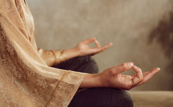 Una persona medita con un kimono dorado y las manos apoyadas sobre las rodillas, en un ejercicio relajante.