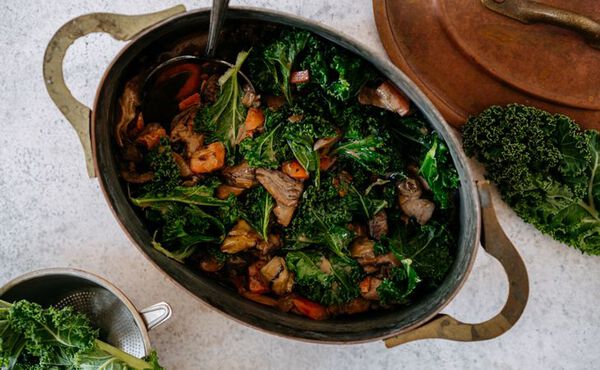 Rustic stew with kale, mushrooms and root vegetables served in a cast iron pot.