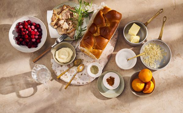 Ingredients for a festive brunch recipe including brioche, cranberries, oranges, and butter on a stone worktop.