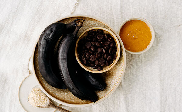 Ingredients for vegan banana ice cream recipe shown in bowls, including overripe bananas, chocolate chips, and peanut butter.