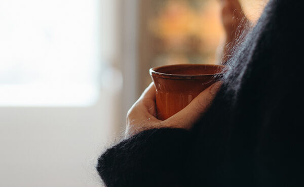 Una persona sostiene una taza de chocolate caliente, disfrutando de un momento de tranquilidad, conexión y propósito durante una ceremonia de cacao.