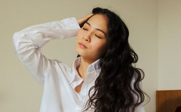 Femme habillée d’une chemise blanche, les yeux fermés, prenant une pause en pleine conscience pour se déconnecter du travail.