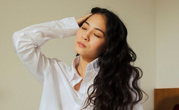 Woman in white shirt with eyes closed taking a mindful pause to switch off from work.