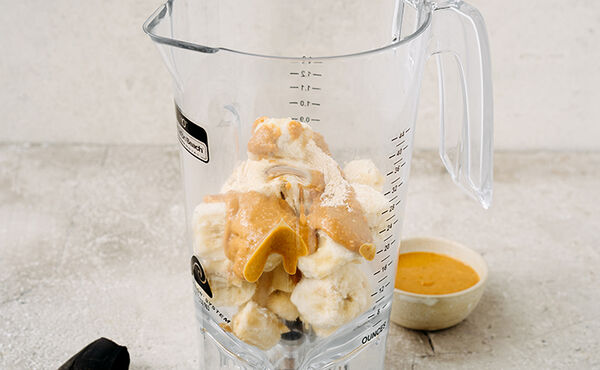 A jug containing frozen banana chunks, peanut butter and cardamom ready to be blended for our vegan banana ice cream recipe.