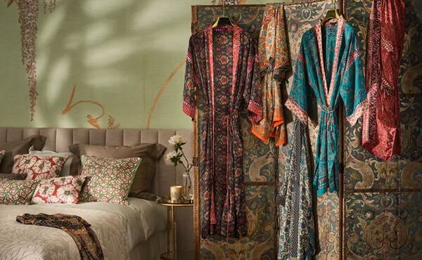 Four House of Rituals silky kimonos featuring colourful decorative hand embroidery, shown hanging up in a cosy bedroom.