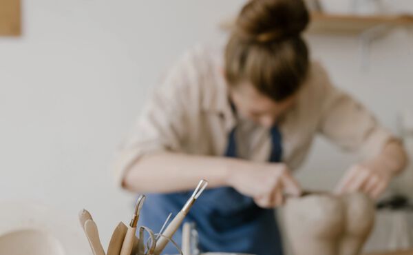 Woman shaping clay while pottery tools in focus on a worktable in the foreground.